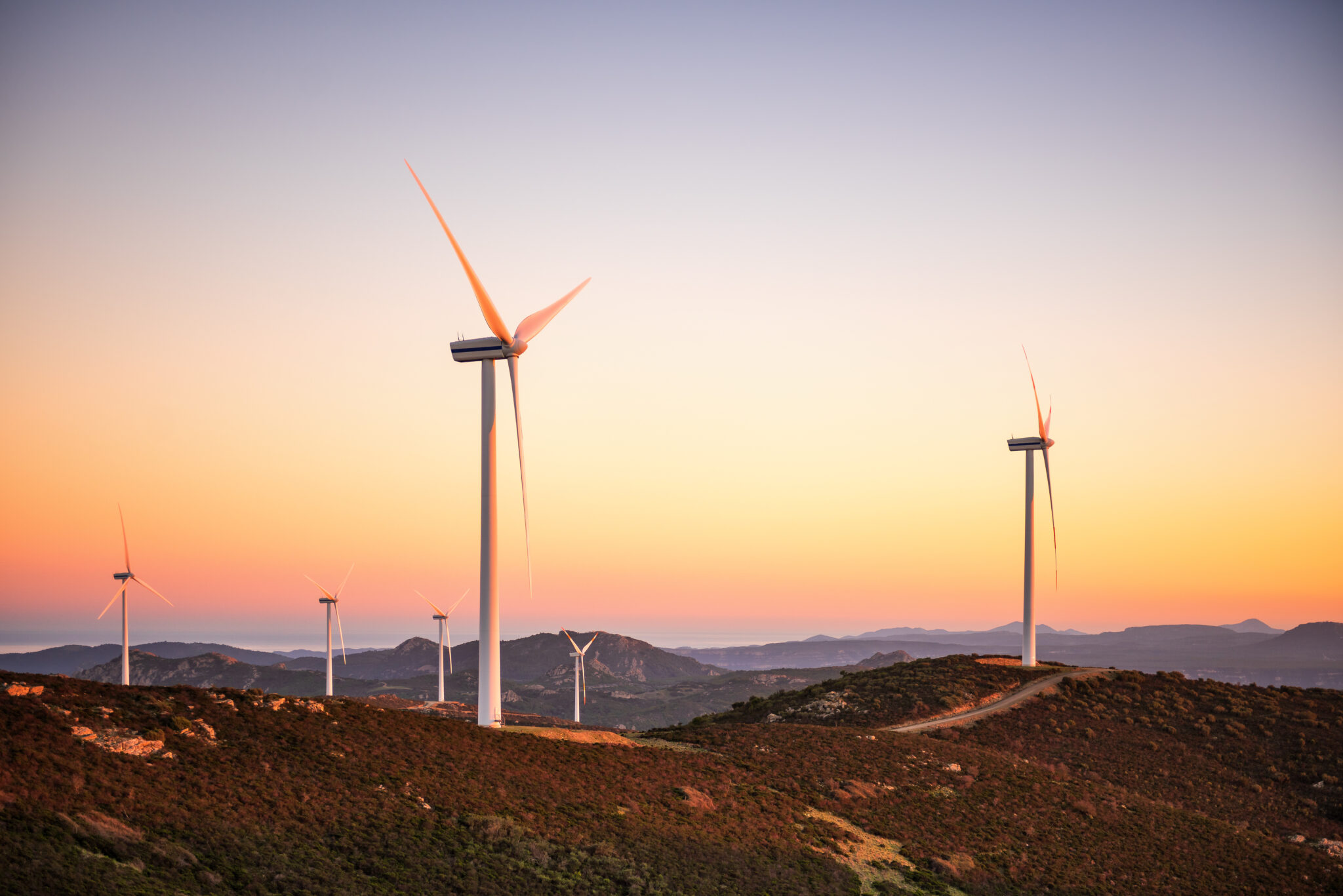 Éoliennes au coucher de soleil sur colline.